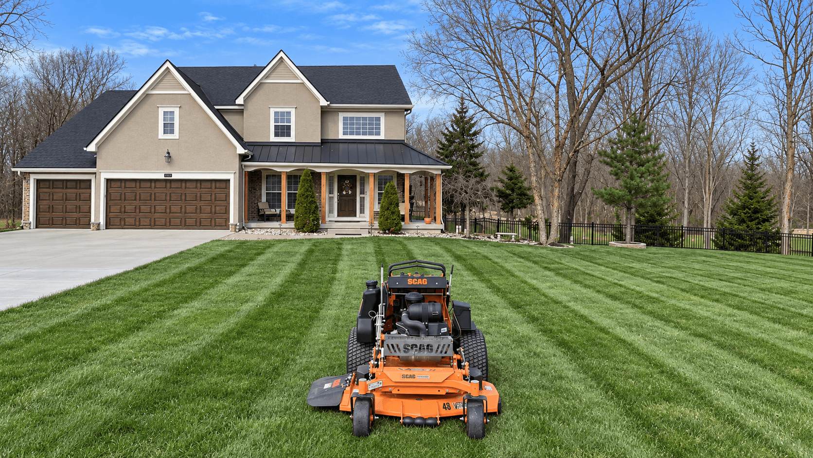 A commercial mower on a striped front lawn with a house and trees behind it